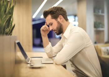 man with hand on temple looking at laptop