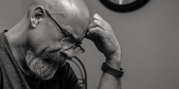 grayscale photo of man thinking in front of analog wall clock