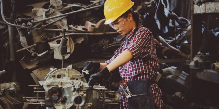 woman wears yellow hard hat holding vehicle part