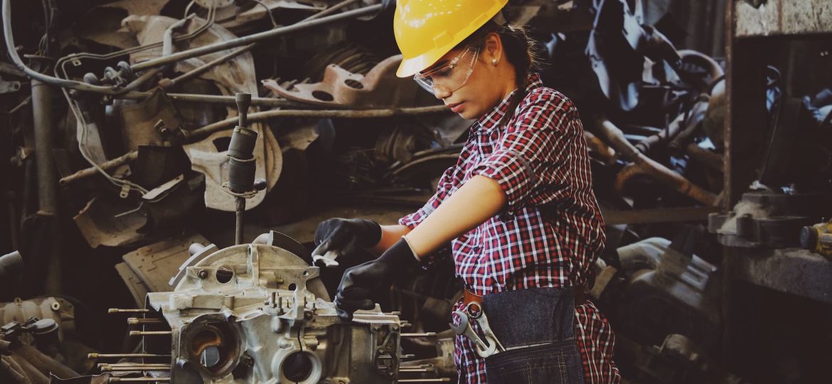woman wears yellow hard hat holding vehicle part